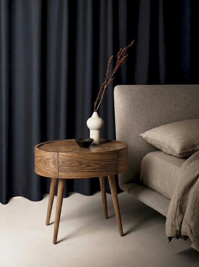 Дизайнерская овальная тумба Ellipse из массива карагача в интерьере современной спальни рядом с кроватью